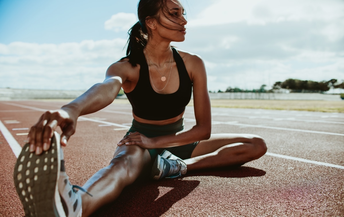 Athlete doing stretching exercises on running track. Woman runner stretching leg muscles