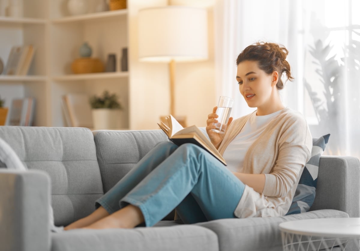 Beautiful young woman enjoying a book sitting on the sofa at home.