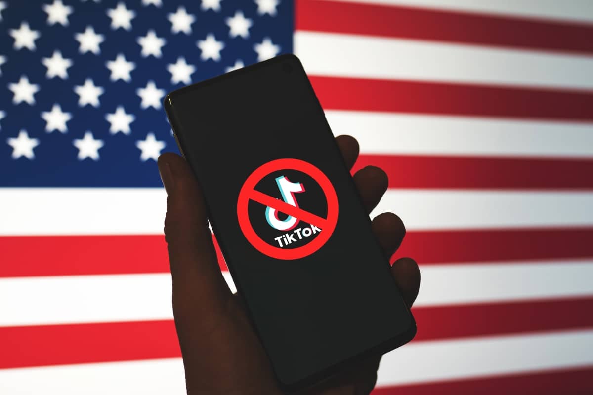 TikTok app logo crossed out with red Ban sign displayed on phone screen with the US flag background. TikTok getting banned in the USA concept.