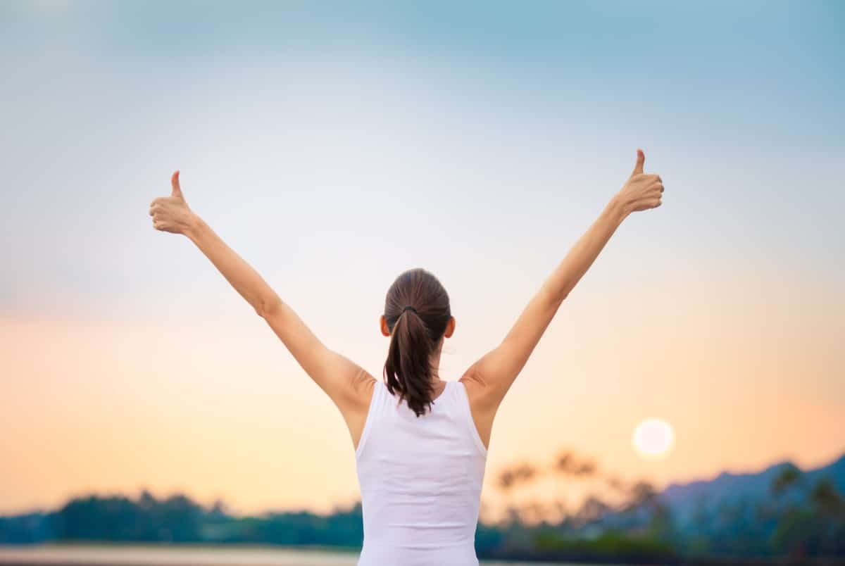 Winning, success and life goals concept. Young woman with arms in the air giving thumbs up.
