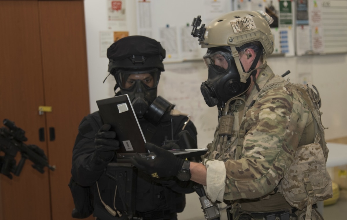 A U.S. Special Operations Forces members and a Qatari Special Forces soldier obtain a computer used in the creation of a crisis scenario during exercise Invincible Sentry
