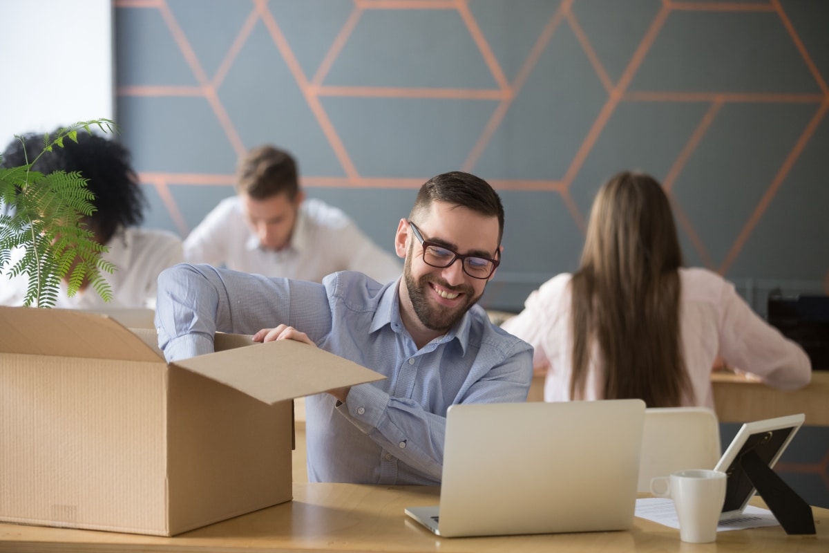 Smiling new male employee unpacking box with belongings at workplace