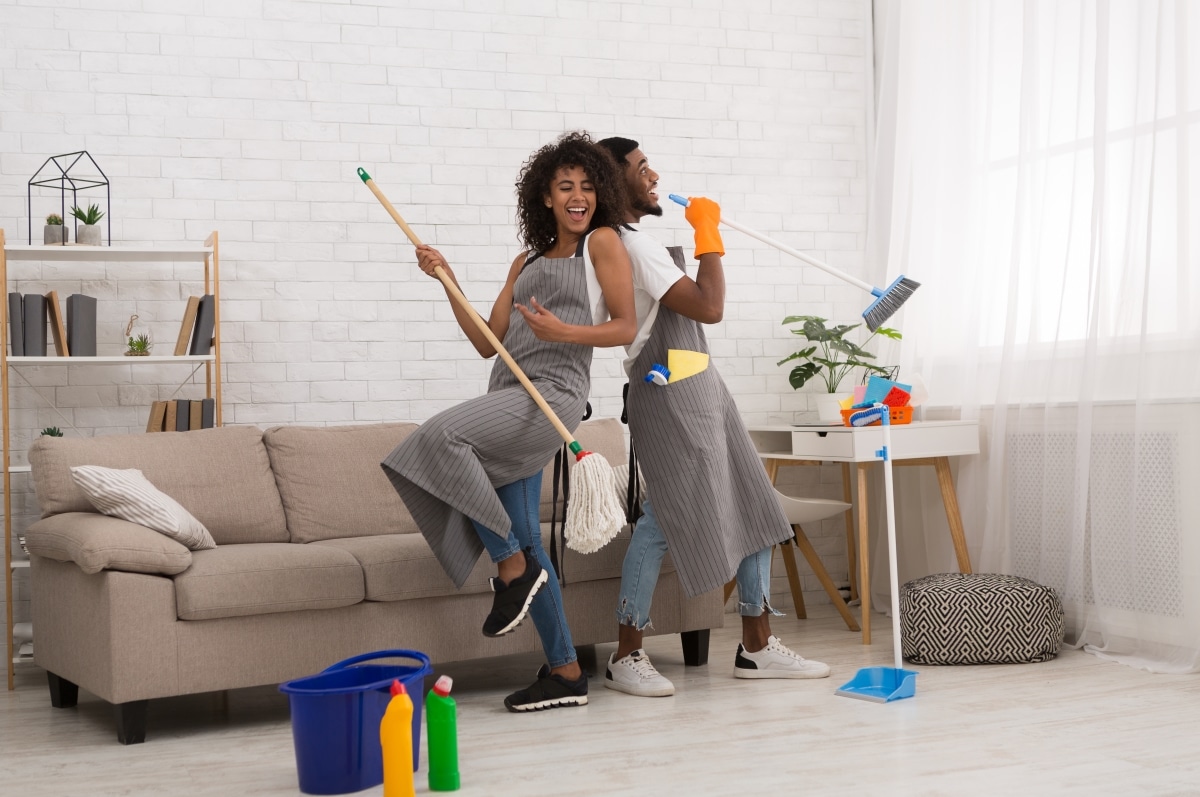 Domestic music band - black man and woman having fun during house cleaning, playing with mop and broom
