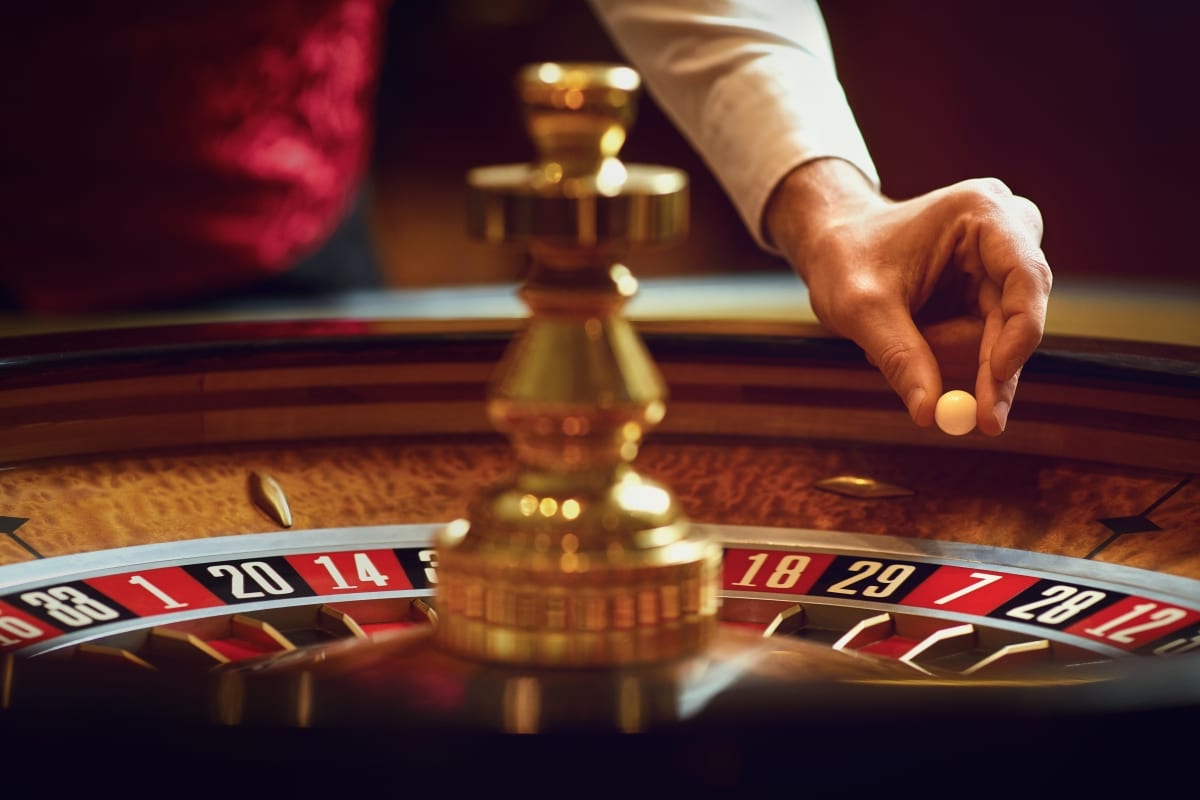 Hand of a croupier with a ball on a roulette wheel during a game in a casino.