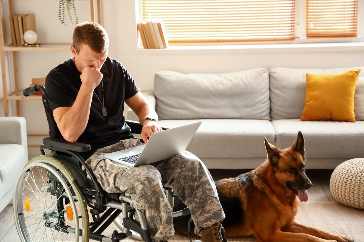 Soldier of USA army in wheelchair with laptop and his dog at home