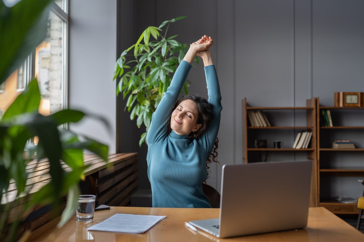 Happy businesswoman warming up body and muscles at workplace, feeling satisfied with work done, smiling female employee resting from computer screen.