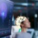 Woman Wearing Brainwave Scanning Headset Sits in a Chair In the Modern Brain Study Laboratory/ Neurological Research Center. Monitors Show EEG Reading and Brain Model.