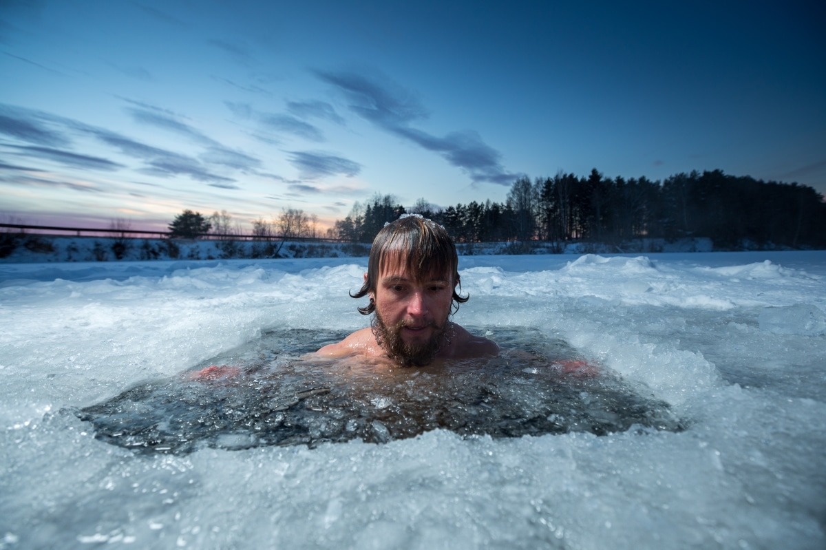 Young man with beard swims in the winter lake