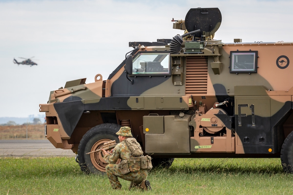 Avalon, Australia - February 27, 2015: Australian Army soldier with a Bushmaster armored personnel carrier (APC) and an Army Eurocopter Tiger helicopter.