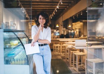 Half length of cheerful Caucaisan entrepreneur feeling success in franchise coffee shop standing in doorway