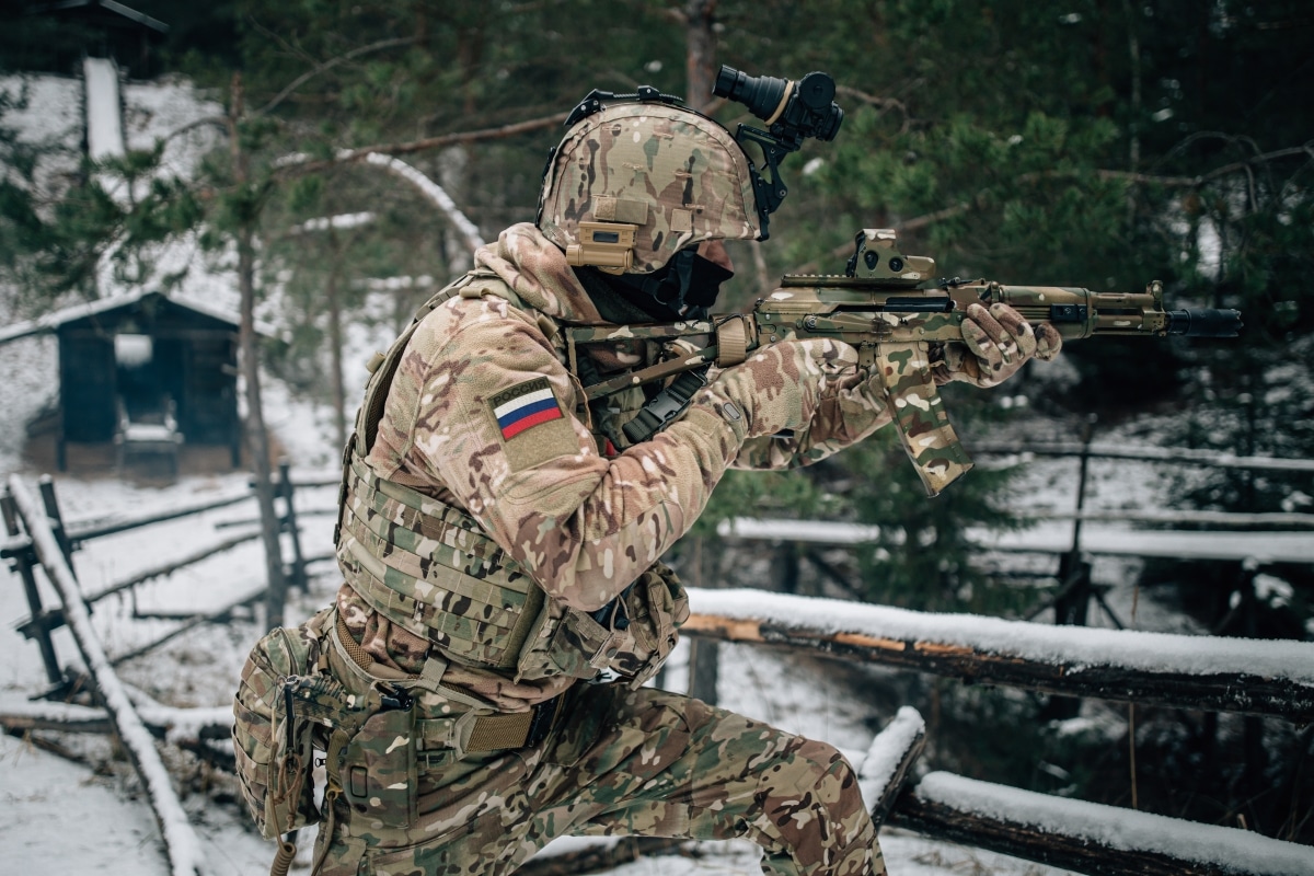 Russian spetsnaz soldier with Kalashnikov tactical assault rifle in camouflage uniform in Dagestan winter mountains. Text translation: Russia.