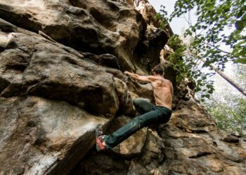 Rock climber climbs bouldering on a cliff on forest. Low angle of strong rock climbing man hanging free on rock with sunflare