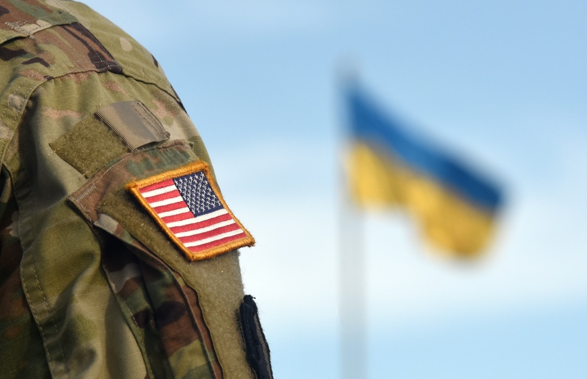 American Flag on Soldiers arm and flag of the Ukraine at background. US military help to Ukraine.