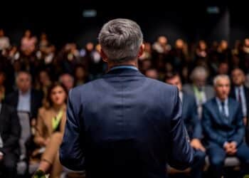 Business man is making a speech in front of a big audience at a conference hall. Speaker giving a talk on corporate business or political conference. Politician talking to group of people