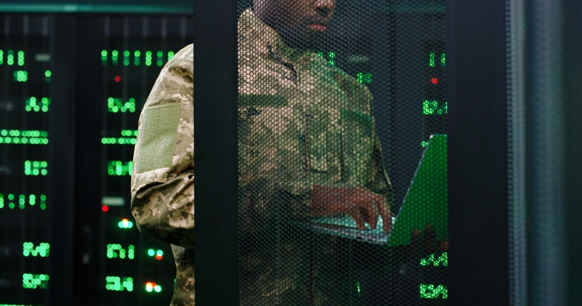 Close up of young African American military officer checking work of servers in analytic monioring center. Man with laptop computer control networking in dark room Cybersecurity in army concept.