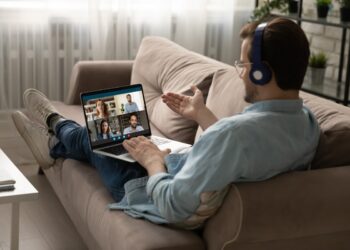Caucasian man in headphone sit on sofa at home talk speak on video call with friends or colleagues. Young male employee in earphones have webcam conference