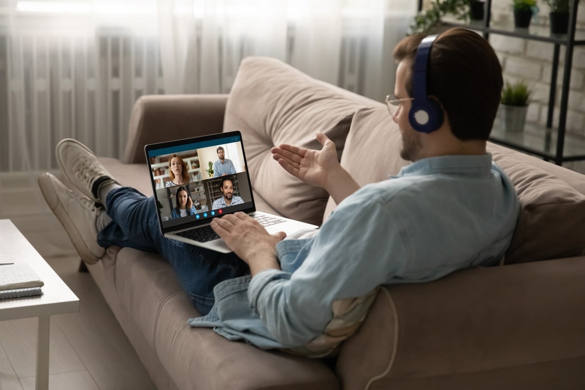 Caucasian man in headphone sit on sofa at home talk speak on video call with friends or colleagues. Young male employee in earphones have webcam conference