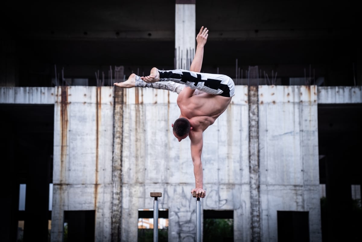 Flexible male circus Artist keep balance by one hand in the concrete structure. Confidence and aspiration concept.