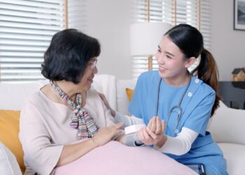 Scrub nurse doctor using digital tonometer check blood pressure for old asia female at home in elderly care cardiovascular medical visit