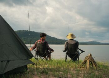 Friendship fisherman or Angler sitting a chair together and camping to fishing at the lake. Camping tent on the shore of the lake. Survival concept.
