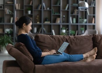 Side view relaxed happy young Indian ethnicity woman working with electronic documents on computer