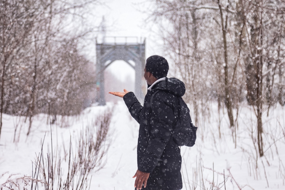 Rear view african american man standing on railway track in snowy winter in countryside forest outside