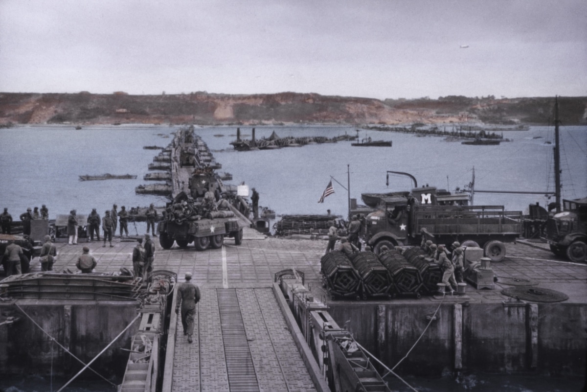 Artificial harbor off Omaha beach in operation before the storm on June 19-22, 1944. Vehicles move from the piers over the causeway to the Normandy shore. B&W Photo with oil color.
