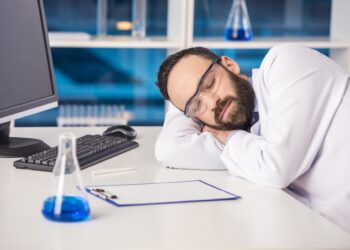 Handsome male scientist sleeping in safety glasses at his workplace in a laboratory.