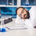 Handsome male scientist sleeping in safety glasses at his workplace in a laboratory.