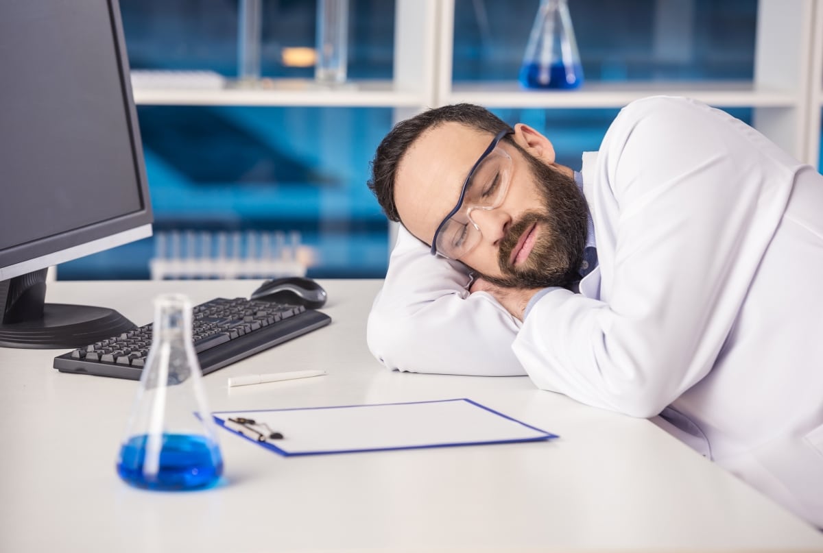 Handsome male scientist sleeping in safety glasses at his workplace in a laboratory.