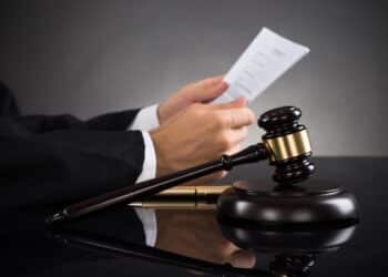 Close-up Of Judge Holding Document With Gavel At Desk