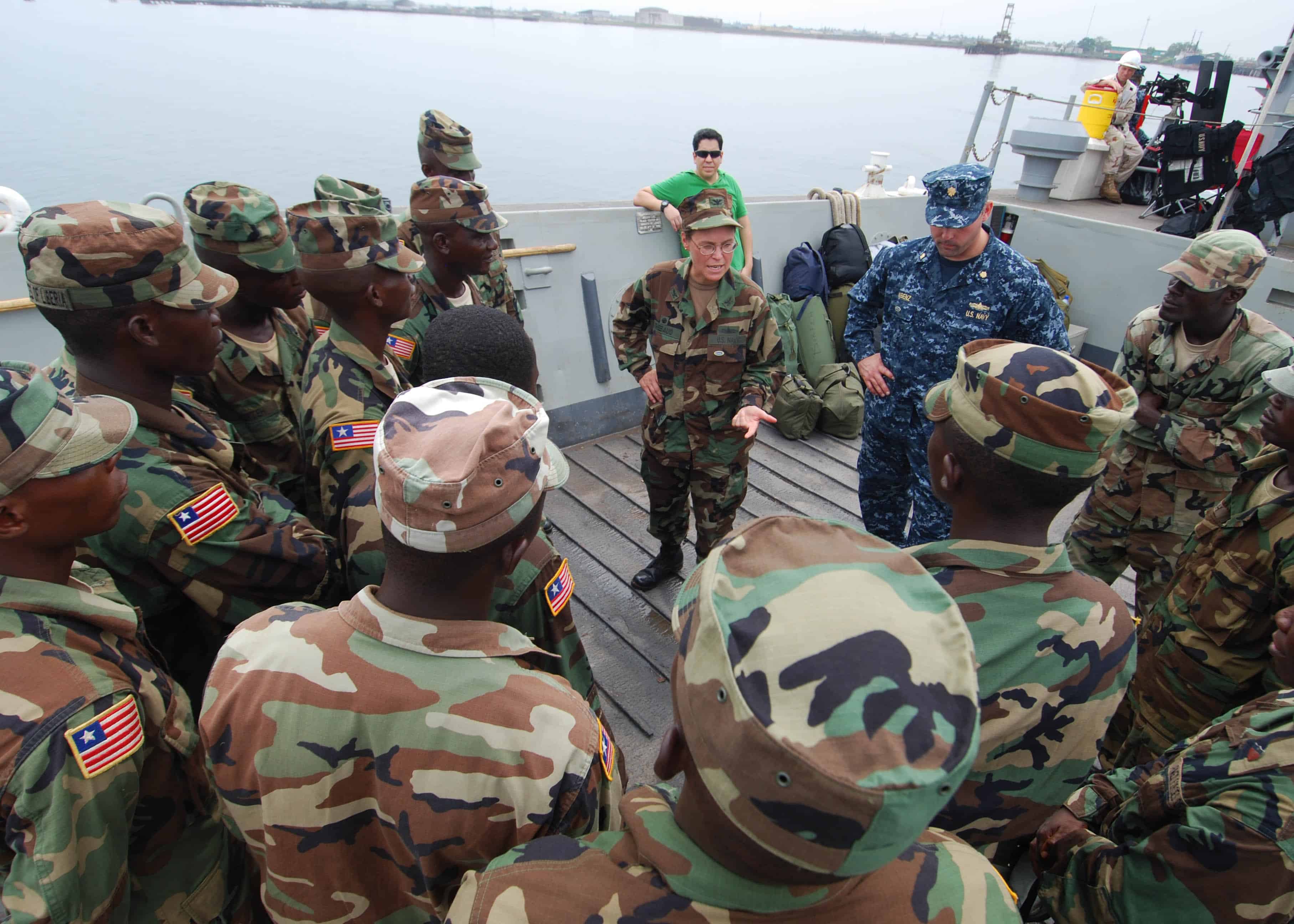 African Partnership Station West Commander, Capt. Cindy Thebaud, and APS Operations Officer, Lt. Cmdr. Timothy Labenz, speak to a group of 17 Armed Forces of Liberia Coast Guardsman while transiting to the Whidbey Island-class amphibious dock-landing ship USS Gunston Hall.