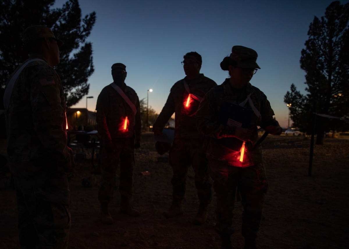 Cadre secure red chemlights to their uniform to enable identification by candidates participating in the night portion of the land navigation course during the Regional Health Command-Central Best Leader Competition, Fort Bliss, Texas, April 11, 2022.