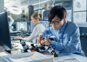 Electronics Engineer Works with Robot Checking Voltage and Program Response time. Computer Science Research Laboratory with Specialists Working.