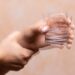 A closeup view on the hands of a person trying to hold a glass of water steady, shaking hands symptomatic of a central nervous and motor system disease such as Parkinson's