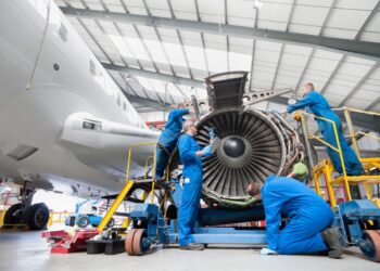 Low-angle wide shot of engineers assembling an engine of a passenger jet at a hangar.