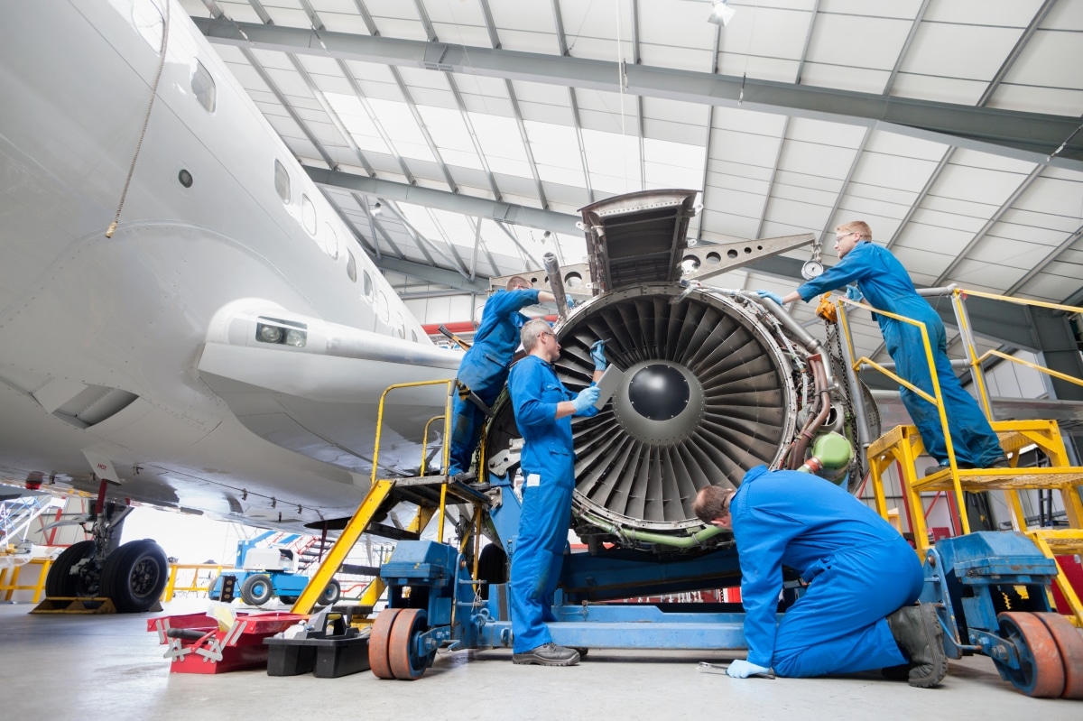Low-angle wide shot of engineers assembling an engine of a passenger jet at a hangar.