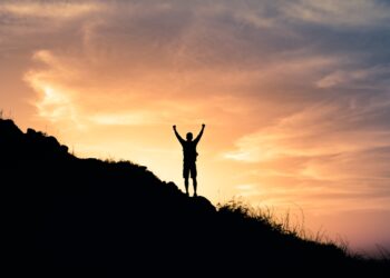Young male hiker standing on a mountain feeling happy and inspired. Adventure, mental strength, and physical health concept.