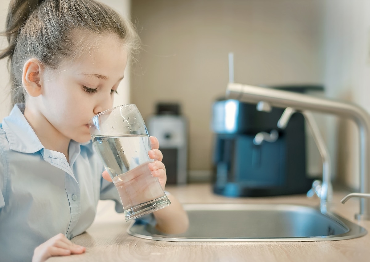 Young caucasian girl is holding a glass with water. Concept of good quality clean water. Kitchen faucet. Pouring fresh drink. Hydration. Healthy lifestyle. World water day. Environmental problem