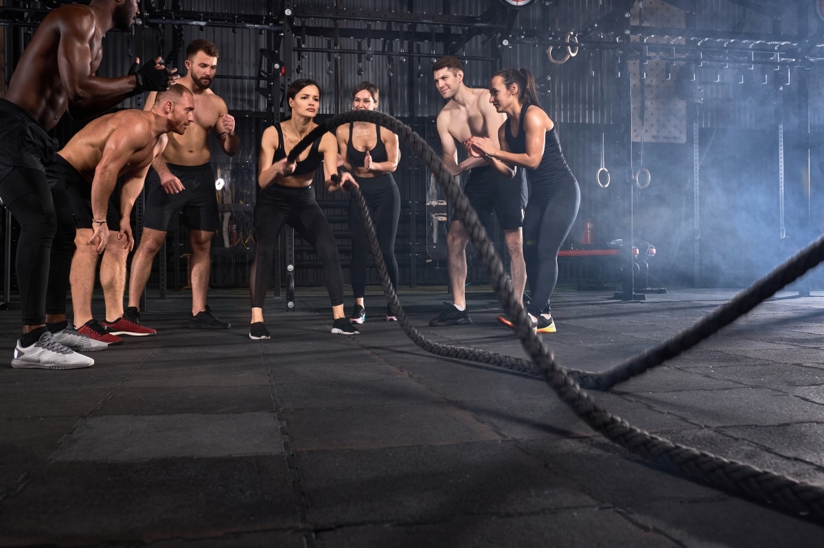 Fit and toned sportswoman in sportive outfit working out in functional training gym doing crossfit exercise with battle ropes. Cross-fit workout motivation, battle rope session concept. copy space