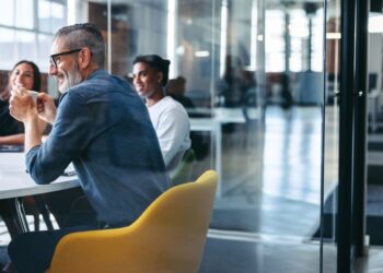 Cheerful mature businessman attending a meeting with his colleagues in an office. Experienced businessman smiling while sitting with his team in a meeting room. Creative businesspeople working together