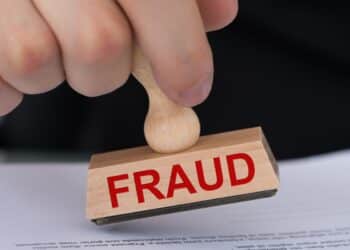 Closeup of hand stamping document with Fraud rubber stamp at table in office