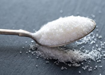 Spoon with white sugar on the dark background