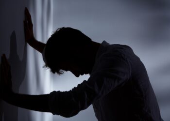 Man leaning with hands against wall, dark room