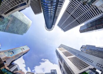 Bottoms-up view of business office skyscrapers and highrise buildings in Singapore's business and financial district at Raffles Place. Fisheye shot of rising architecture into blue and cloudy skies.