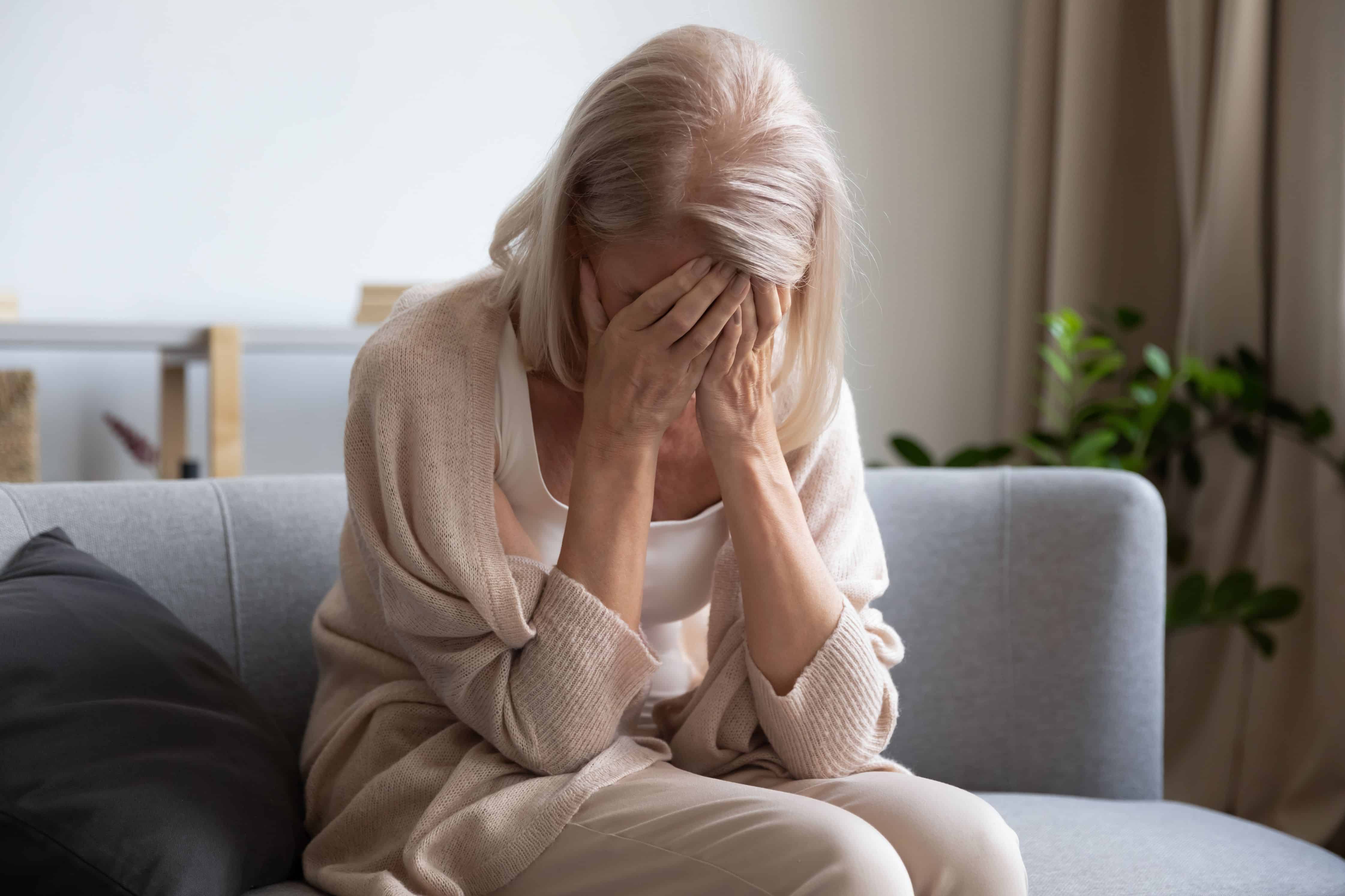 Depressed older woman covering face with hands, crying, feeling desperate. Unhappy mature grandmother experiencing grief, relative’s death, bad news. Stressed elder lady suffering from loneliness.