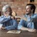 Happy elderly dad and grownup son giving fist bumps, making friends gesture, celebrating achievement in boardgame, expressing respect, playing checker draughts, enjoying hobby, leisure time