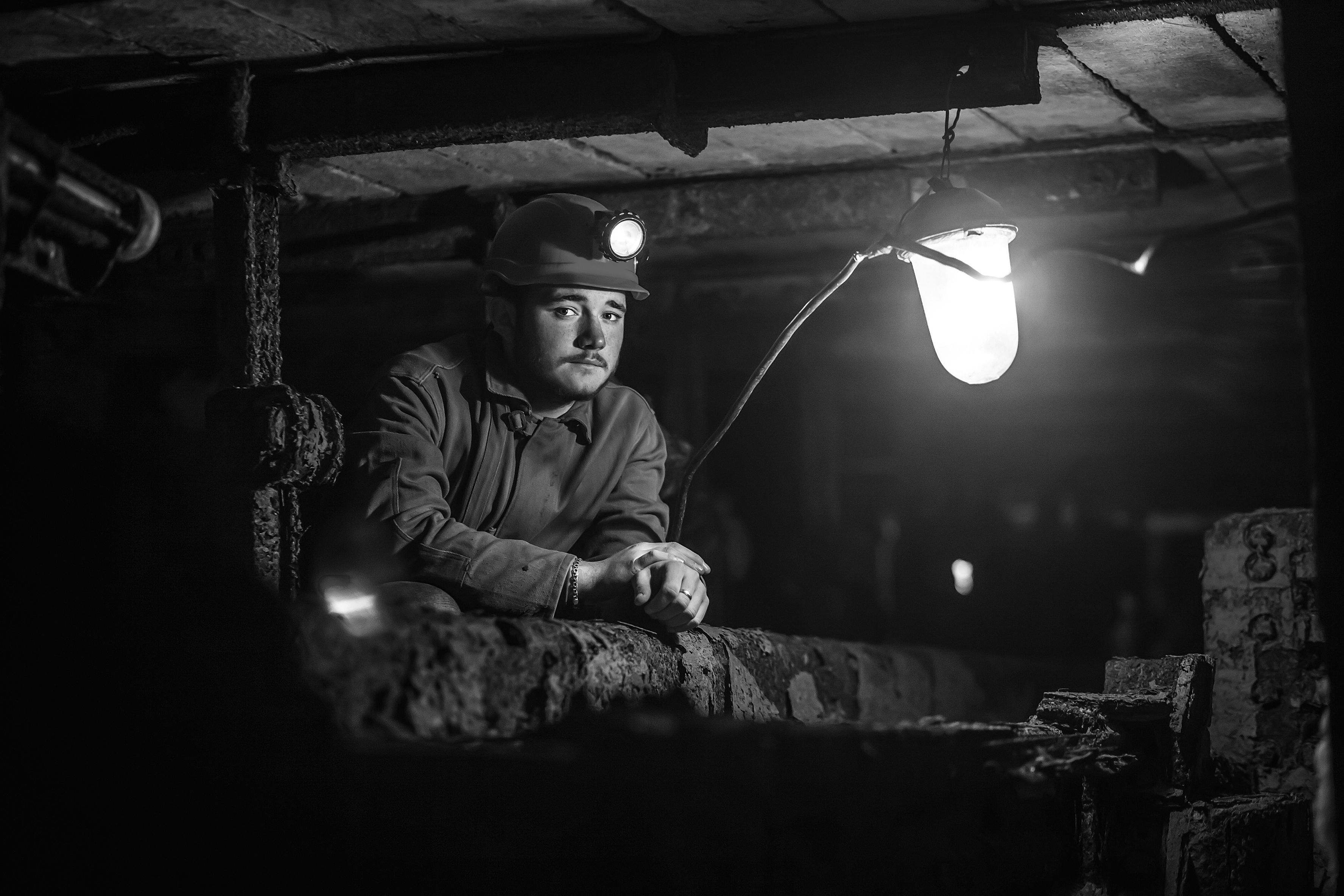 Tired young miner in an old coal mine. A miner in a protective suit with a helmet on his head and a flashlight works in the dark. Work in a coal mine.