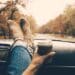 Woman feet in warm socks on car dashboard. Drinking take away coffee on road. Fall trip. Rain drops on windshield. Freedom travel concept. Autumn weekend.