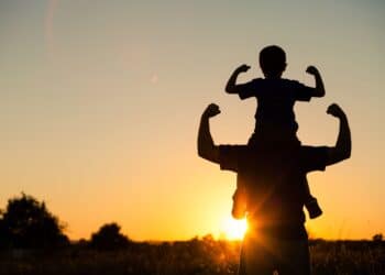 Father and son playing in the park at the sunset time. People having fun on the field. Concept of friendly family and of summer vacation.
